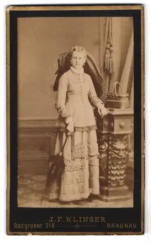 Fotografie J. F. Klinger, Braunau, Stadtgragen 318, Portrait Dame im hellen Kleid mit grosser Haarschleife und Schirm