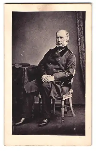 Fotografie Fotograf und Ort unbekannt, Portrait älterer Herr im Anzug mit Backenbart sitzend im Atelier