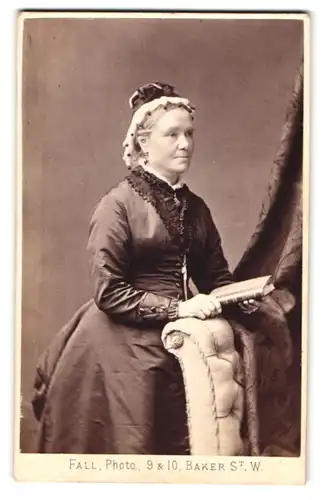 Fotografie T. Fall, London, Baker St. 9 /10, Portrait ältere Dame im seidenen Kleid mit Hut und Buch in der Hand