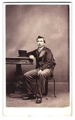 Fotografie Melliss, Liverpool, Bold Street 120, Portrait Herr im Anzug mit Stock und Zylinder auf dem Tisch