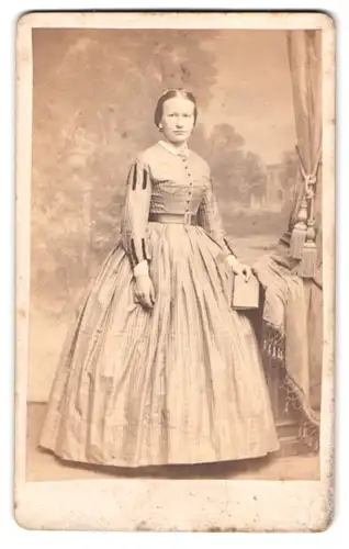 Fotografie Fotograf und Ort unbekannt, Portrait junge Frau im gestreiften Kleid vor einer Studiokulisse
