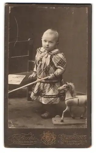 Fotografie J. Fuchs, Dresden, Waisenhaus Strasse 16, Portrait kleines Mädchen im karierten Kleid mit Spielzeugpferd