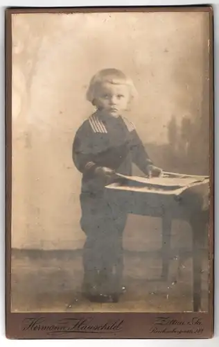 Fotografie Hermann Hauschild, Zittau i. Sa, Reichenbergerstrasse 28, Portrait kleiner Junge im Matrosenanzug mit Zeitung