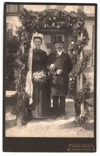 Fotografie Atelier Reich, Augustenburg, Portrait eines elegant gekleideten Paares mit Schleier und Blumenstrauss