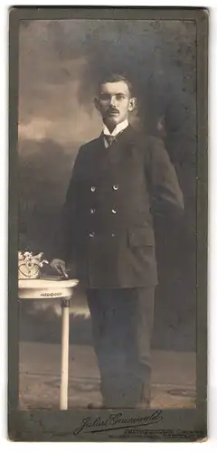 Fotografie Julius Grunewald, Oberneukirch, Portrait stattlicher Herr im Anzug an einem Tisch stehend
