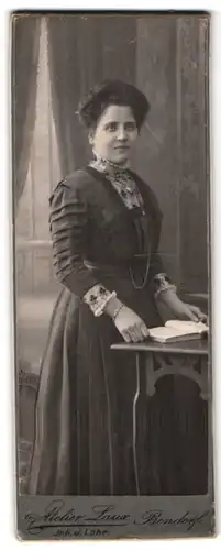Fotografie Atelier Laux, Bendorf, Portrait einer elegant gekleideten Frau mit Buch am Tisch stehend