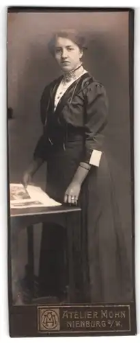 Fotografie Atelier Mohn, Nienburg a. W., Portrait brünette junge Schönheit mit Zeitschrift am Tisch stehend