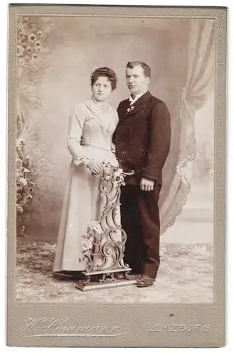 Fotografie H. Hemmann, Lenzburg, Bahnhofstr., Portrait Eheleute im hellen Kleid und Anzug mit Locken vor Studiokulisse