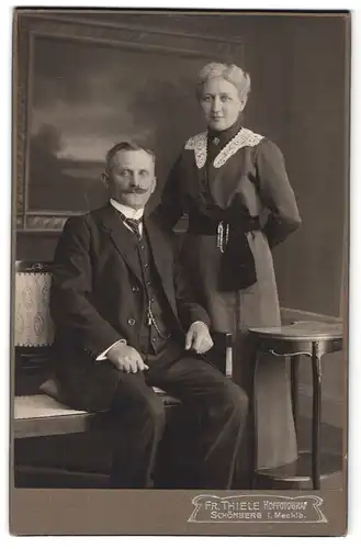 Fotografie Fr. Thiele, Schönberg i. M., Portrait älterer Mann und Frau im Biedermeierkleid und Anzug vor Studiokulisse
