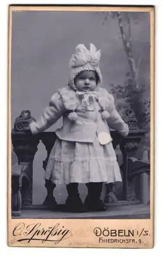 Fotografie O. Sprössig, Döbeln, Friedrichstr. 9, Portrait Kleinkind im Winterkleid mit Wollmütze und Schleife