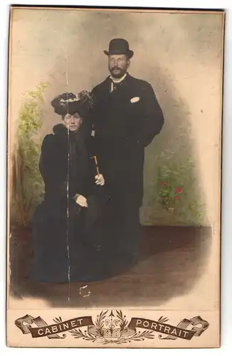 Fotografie Cabinet Portrait, Ort unbekannt, Bürgerlicher mit Melone und Frau mit Kopfschmuck und Stock