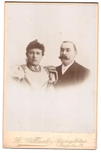 Fotografie H. Wittrock, Hamburg, Langereihe 54, Portrait Mann und Frau im Anzug mit Walrossbart und Kleid mit Locken