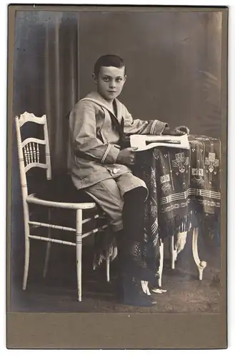 Fotografie unbekannter Fotograf und Ort, Portrait Knabe in Marinekleidern am Tisch sitzend