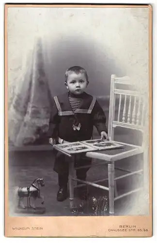 Fotografie Wilhelm Stein, Berlin, Chaussee Strasse 65-66, Portrait kleiner Junge im Matrosenanzug mit einem Album