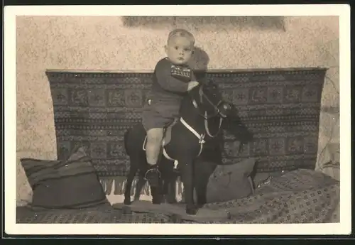 Fotografie niedlicher Knabe auf Spielzeug-Pferd sitzend