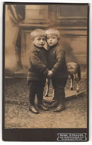 Fotografie Gebr. Strauss, München, Neuhauserstrasse 20, Portrait zwei modisch gekleidete Jungen mit Spielzeugpferd