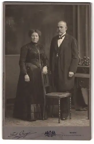 Fotografie Ferd. Grega, Wien, Stefaniestrasse 7, Portrait älteres Paar in hübscher Kleidung