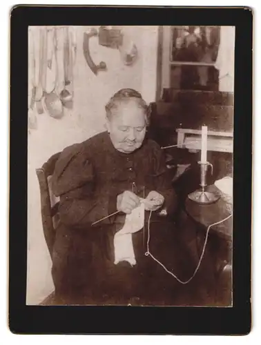 Fotografie unbekannter Fotograf und Ort, Portrait ältere Dame beim Stricken am Tisch mit Kerze