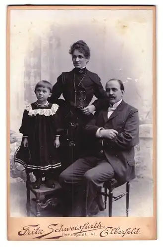 Fotografie Fritz Schweisfurth, Elberfeld, Herzogstr. 41, Portrait Familie mit Tochter im schwarzen Kleid auf einem Stuhl