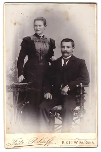 Fotografie Fritz Rohloff, Kettwig / Ruhr, Portrait Frau und Mann im Biedermeierkleid mit Brosche und Anzug, Schnauzbart