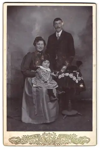 Fotografie unbekannter Fotograf und Ort, Portrait Mutter und Vater mit Tochter im karierten Kleid posieren im Atelier