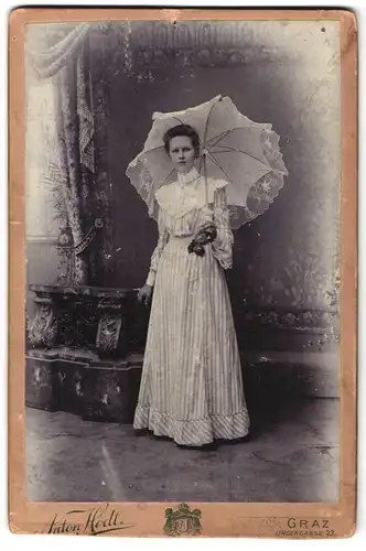 Fotografie Anton Hödl, Graz, Ungergasse 23, Portrait junge Frau im gestreiften Kleid mit Schirm vor einer Studiokulisse