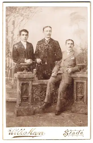 Fotografie Wilh. Meyer, Stade, Portrait drei junge Herren im Anzug mit Zigarre