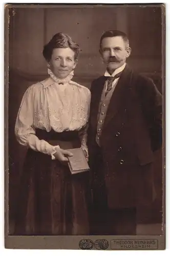 Fotografie Theodor Reinhard, Hildesheim, Portrait älteres Paar in hübscher Kleidung mit Buch