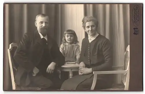 Fotografie J. N. Kreutzer Nchf., Kaufbeuren, Portrait bürgerliches Paar mit Tochter am Tisch