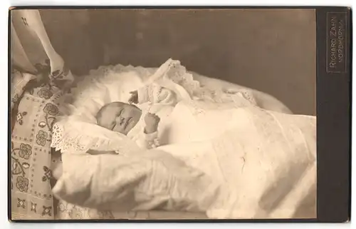 Fotografie Richard Zahn, Nordhorn i. H., schlafendes Kleinkind in seiner Wiege