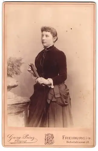 Fotografie Georg Prinz, Freiburg i. B., Hebelstr. 10, Portrait junge Frau im samtenen Kleid mit Fächer und Locken