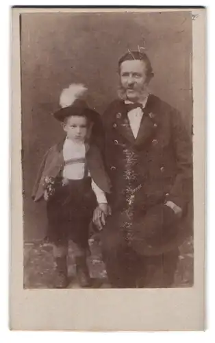 Fotografie unbekannter Fotograf und Ort, Portrait Vater im Anzug mit kleinem Sohn in Tracht mit Federhut