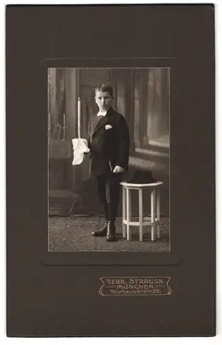 Fotografie Gebr. Strauss, München, Neuhauserstr. 20, Portrait junger Knabe im Anzug mit Kerze, Kommunion