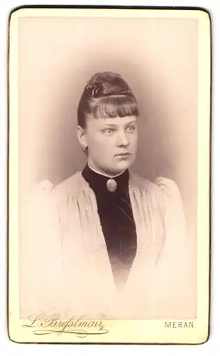 Fotografie L. Bresslmair, Meran, Portrait bildschöne junge Frau mit Dutt und Brosche am Blusenkragen