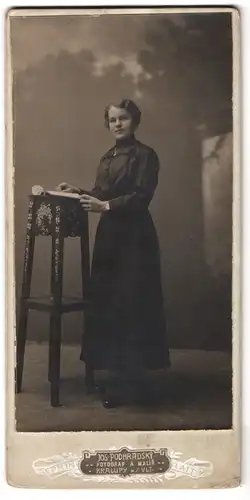 Fotografie Jos. Podhradsky, Kralup, Portrait junge Frau im dunklen Seidenkleid steht an einem Pult