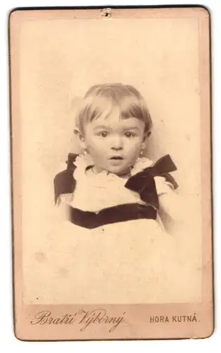 Fotografie Bratie Vyborny, Kuttenberg, Portrait Kleinkind im weissen Kleid mit Schleifen und Ohrringen