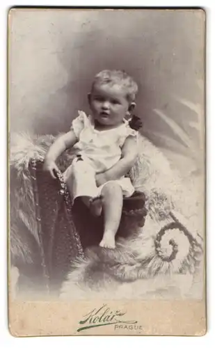 Fotografie Kolar, Prag, Portrait Kleinkind im weissen Kleid mit Schleife sitzt auf einem Fell