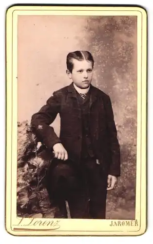 Fotografie L. Lorenz, Jaromer, Portrait junger Knabe im karierten Anzugm mit Hut lehnt an einem Stein