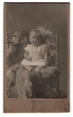 Fotografie Vaclav Halla, Louny, Komenskeho nam., Portrait Kleinkind im weissen Leibchen auf einem Fell sitzend