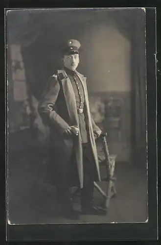 AK Uniformfoto, junger Offizier steht an einem Stuhl, im Mantel mit Schirmmütze