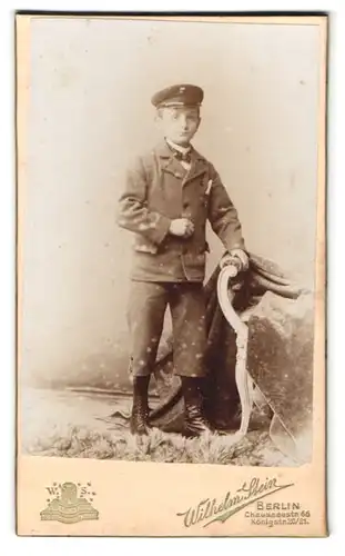 Fotografie Wilhelm Stein, Berlin, Chausseestr. 66, Portrait frecher Bube mit Schirmmütze, Anzug und Schnürstiefel
