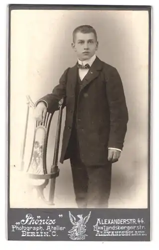 Fotografie Atelier Phönix, Berlin, Alexanderstr. 44, Portrait junger Mann elegant im Anzug am Stuhl stehend