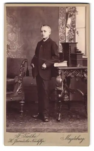 Fotografie F. Tiedke, Magdeburg, Kaiserstr. 94, Portrait blonder Bube im Anzug an einem Tisch stehend