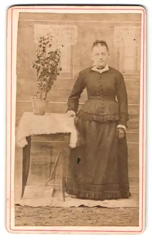 Fotografie unbekannter Fotograf und Ort, Portrait einer elegant gekleideten Frau am Tisch stehend