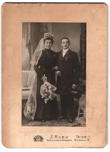 Fotografie J. Ruby, Trier, Brückenstrasse 76, Portrait junges Paar in Hochzeitskleidung mit Schleier und Blumenstrauss