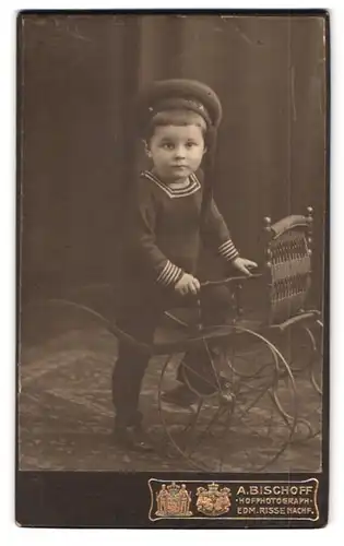 Fotografie A. Bischoff, Bochum, Friedrichstr. 36, Portrait junger Knabe im Matrosenanzug mit besteigt einen Puppenwagen