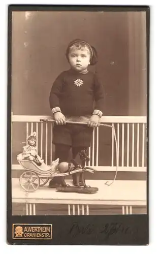 Fotografie A. Wertheim, Berlin, Oranienstr., Portrait kleiner Junge mit Puppenwagen und Zipfelmütze