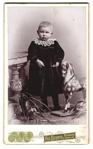 Fotografie Frz. Herber, Duisburg, Poststr. 36, Portrait Kleinkind im Samtkleid mit geflecktem Schaukelpferd