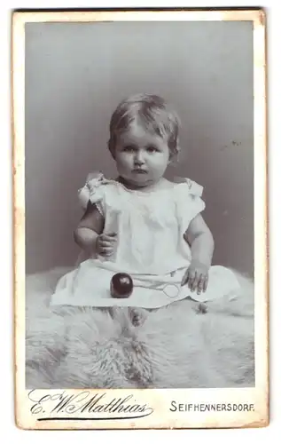 Fotografie E. W. Matthias, Seifhennersdorf in Sachsen, Portrait süsses Kleinkind im weissen Kleid mit Ball