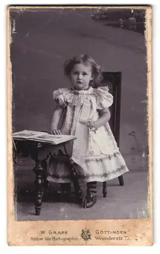 Fotografie W. Grape, Göttingen, Weenderstrasse 75, Portrait kleines Mädchen im Kleid mit Bilderbuch